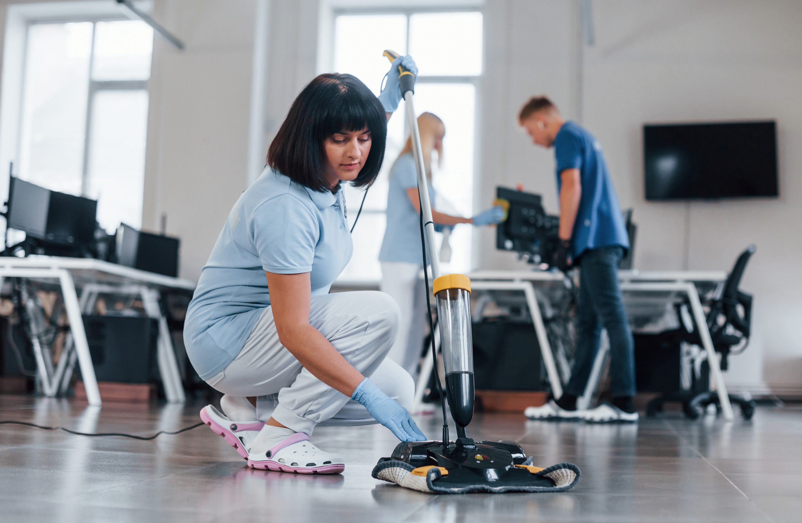 woman uses vacuum cleaner. group of workers clean modern office together at daytime