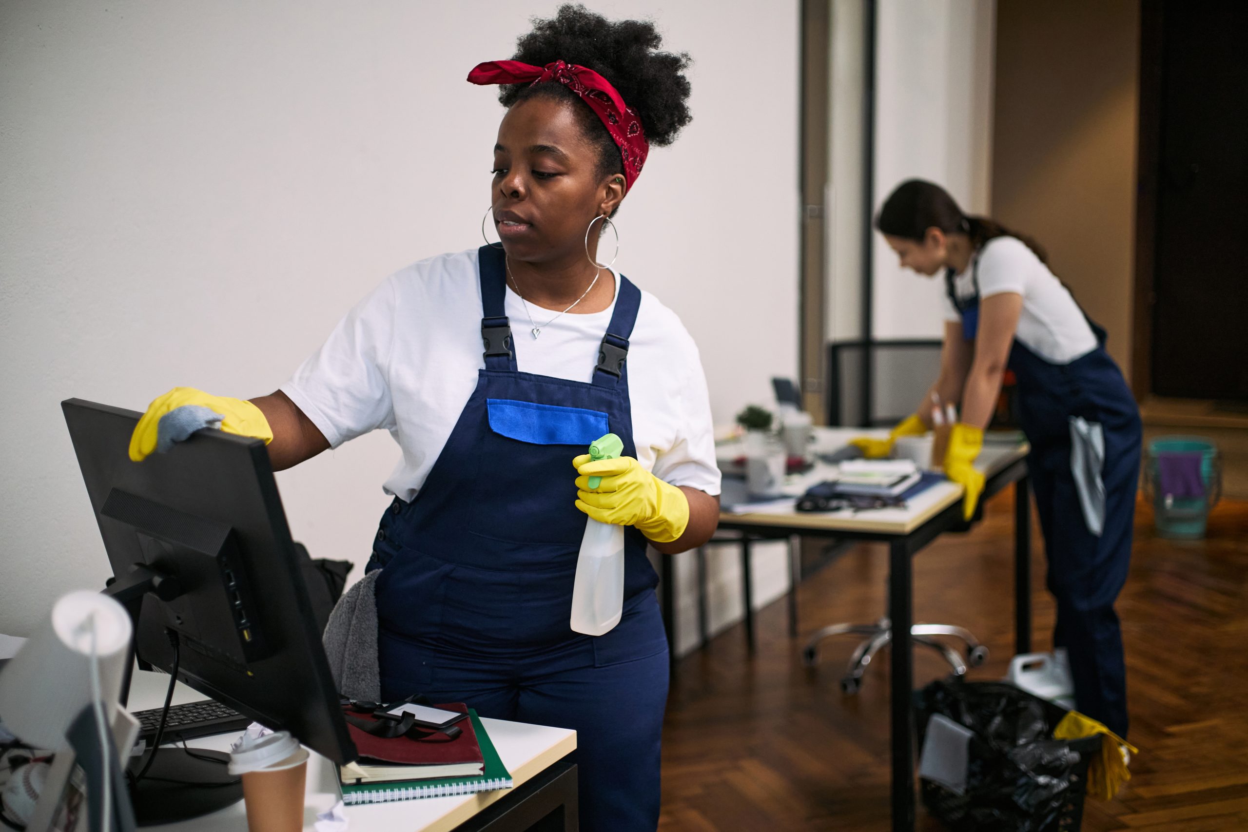 young black woman cleaning computer monitor while coworker organizing office desk
